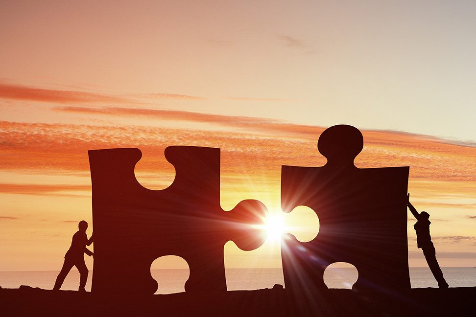 Two people joining giant puzzle pieces at sunset